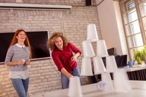 Pyramida z bílých kelímků a dva smějící se soutěžící v zasedací místnosti